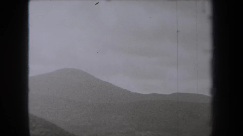 1938 New York home-movie frame showing layered hills under a heavy gray sky, bordered by dark film edges.
