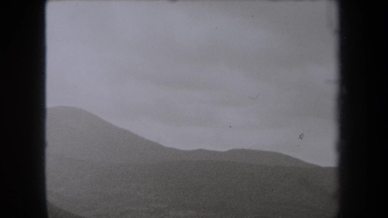 Soft mountain ridge and cloudy sky framed by dark film borders.