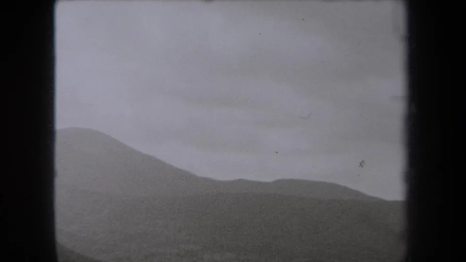 Black-and-white 8mm frame of a New York hillside view, with layered slopes and a muted overcast sky.