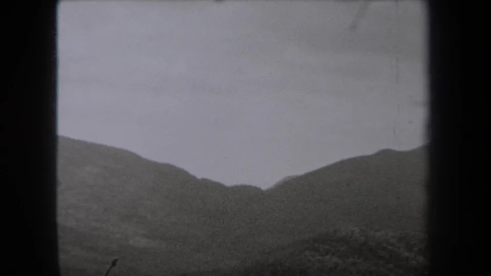 Black-and-white 8mm view of rounded New York hills beneath a pale cloudy sky, with dark frame edges visible.
