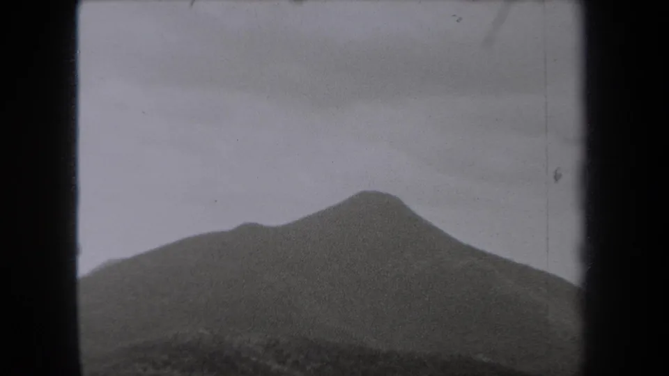1938 New York 8mm frame with a rounded mountain peak emerging from fog beneath a flat gray sky.