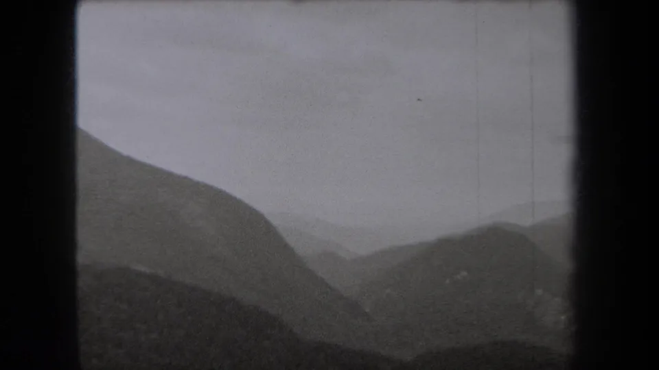 1938 New York 8mm frame showing layered mountain slopes and a hazy valley under gray cloud cover.