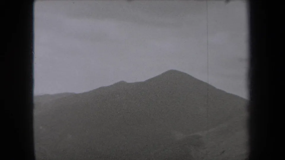 1938 New York 8mm frame of a broad, dark mountain ridge beneath low gray cloud and atmospheric haze.