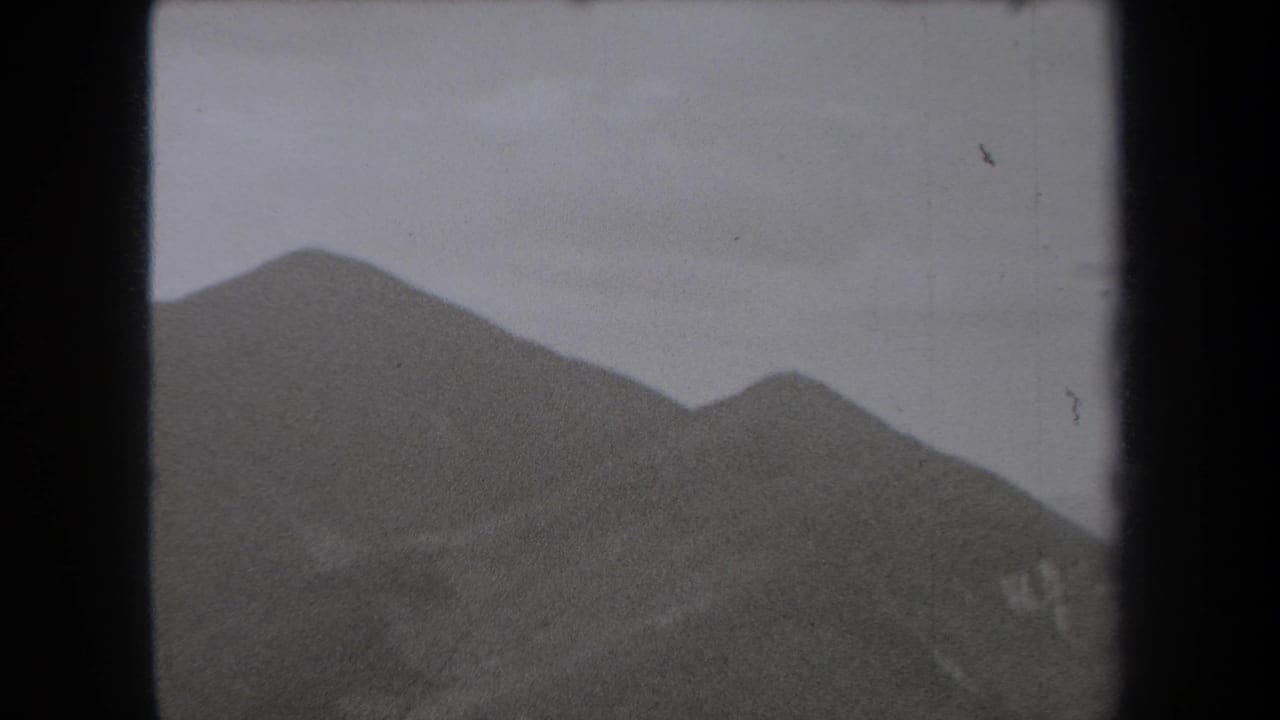 1938 New York 8mm frame showing rounded mountain peaks under a pale partly cloudy sky, with soft grain and gate-edge shadowing.