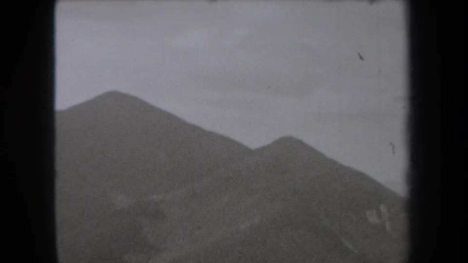 1938 New York 8mm frame showing rounded mountain peaks under a pale partly cloudy sky, with soft grain and gate-edge shadowing.