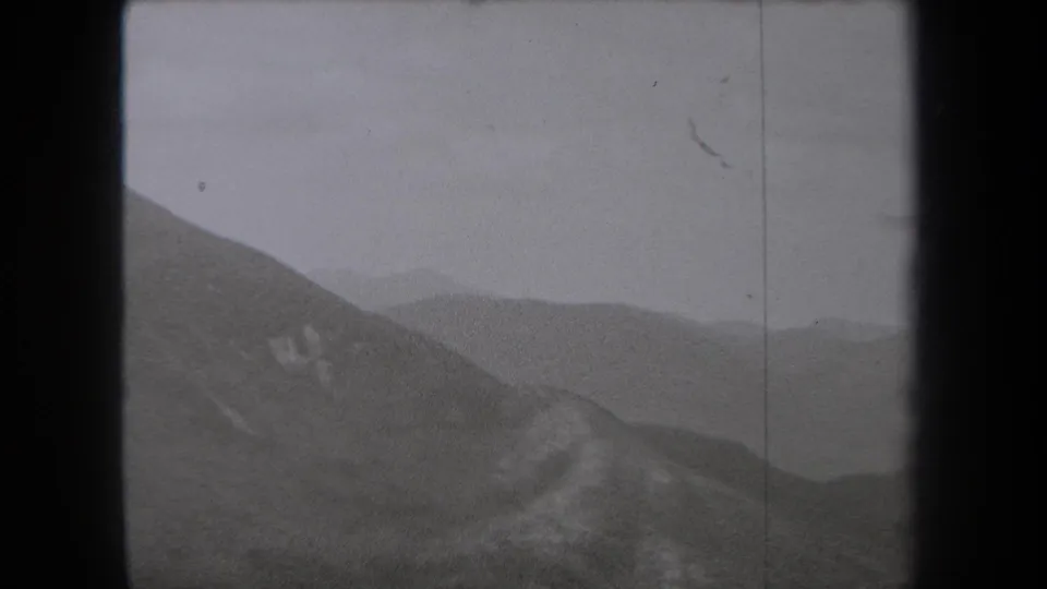 1938 New York 8mm landscape frame showing a sloping mountain foreground, pale rock patches, and distant ridges receding into haze.
