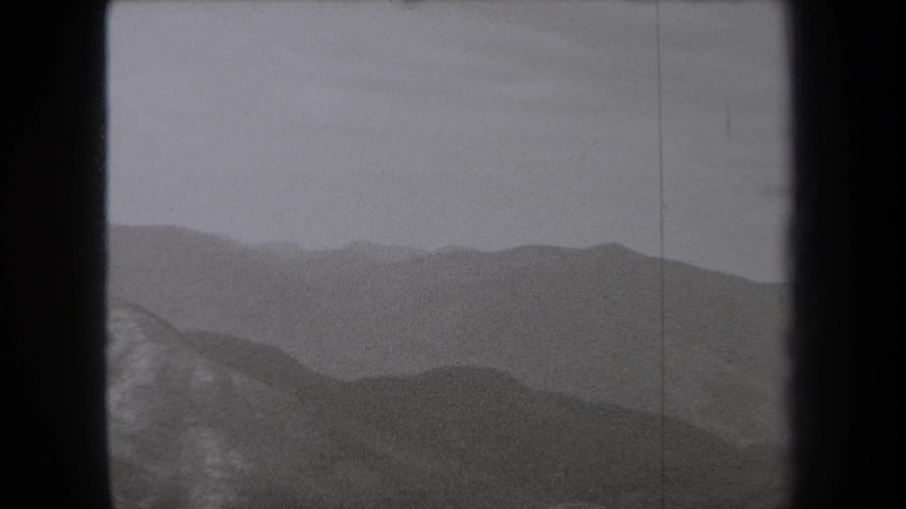1938 New York 8mm frame showing layered mountain ridges fading into haze beneath a pale sky.
