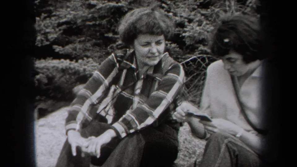 Black-and-white 1938 New York home-movie frame of two women seated outdoors, looking down together at a small hand-held item.