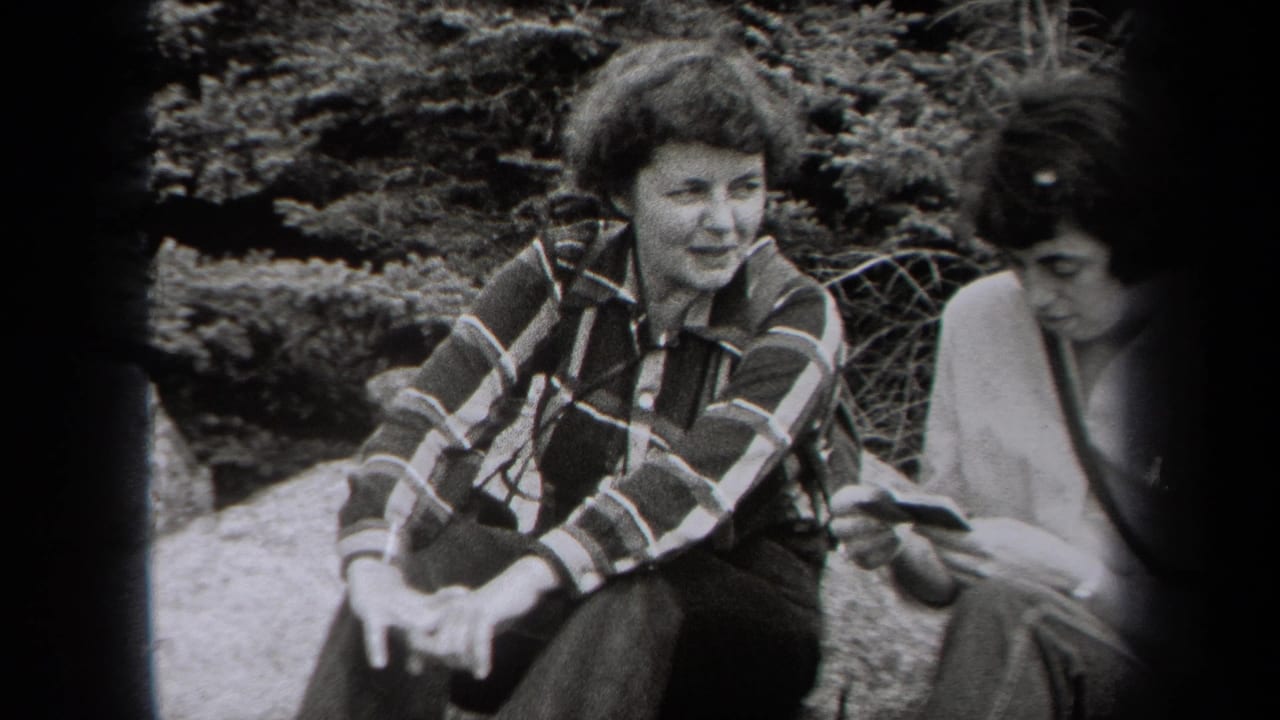 In metadata-supported 1938 New York footage, two women sit outdoors near shrubs, with one smiling in a plaid shirt and the other looking down.