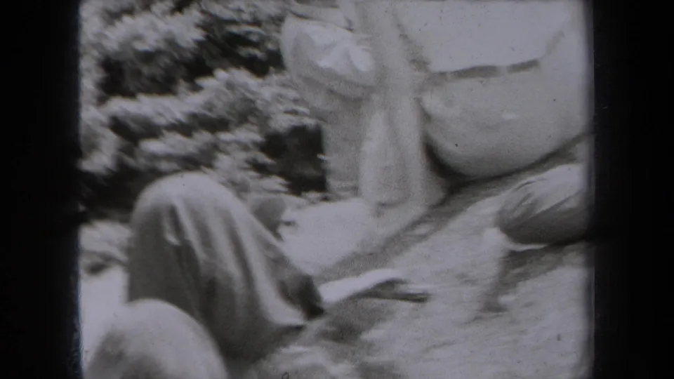 1938 New York home-movie frame showing family members seated near rocks and trees on an outdoor overlook.