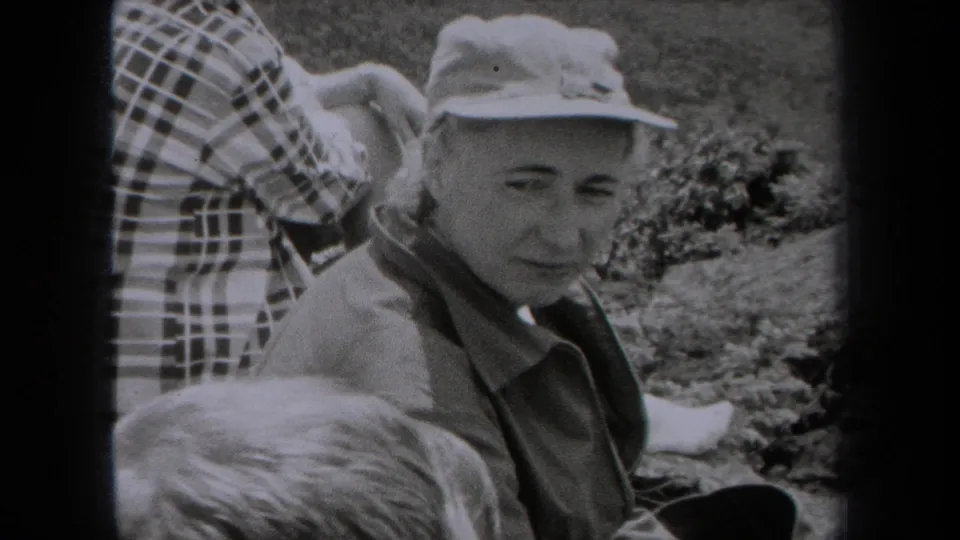 An older woman in a light cap and jacket sits with family on a grassy New York overlook in 1938 home-movie footage.