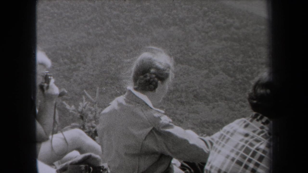 1938 New York home-movie frame showing adults seated outdoors on grass, their faces partly turned from the camera.