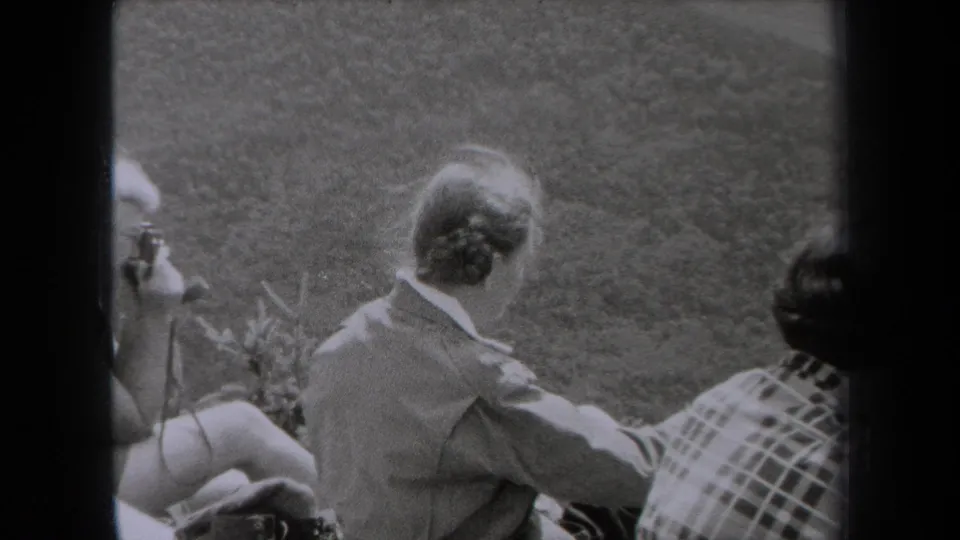 1938 New York home-movie frame showing adults seated outdoors on grass, their faces partly turned from the camera.