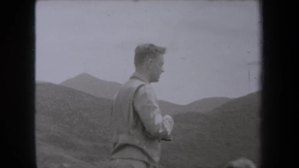 In 1938 New York home-movie footage, a man in a vest stands in profile against rugged mountain terrain.