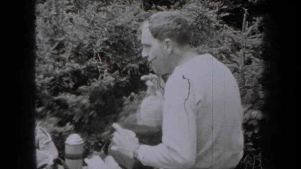 In this 1938 New York 8mm frame, the seated man appears to eat or drink while surrounded by dense evergreen foliage.