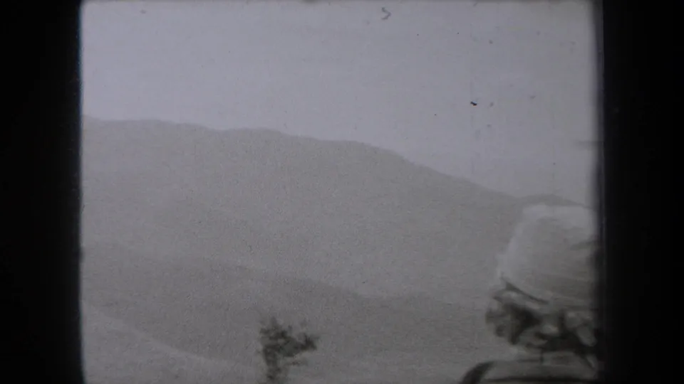 1938 New York home-movie frame showing a hat-wearing figure from behind near hazy, layered sand dunes.