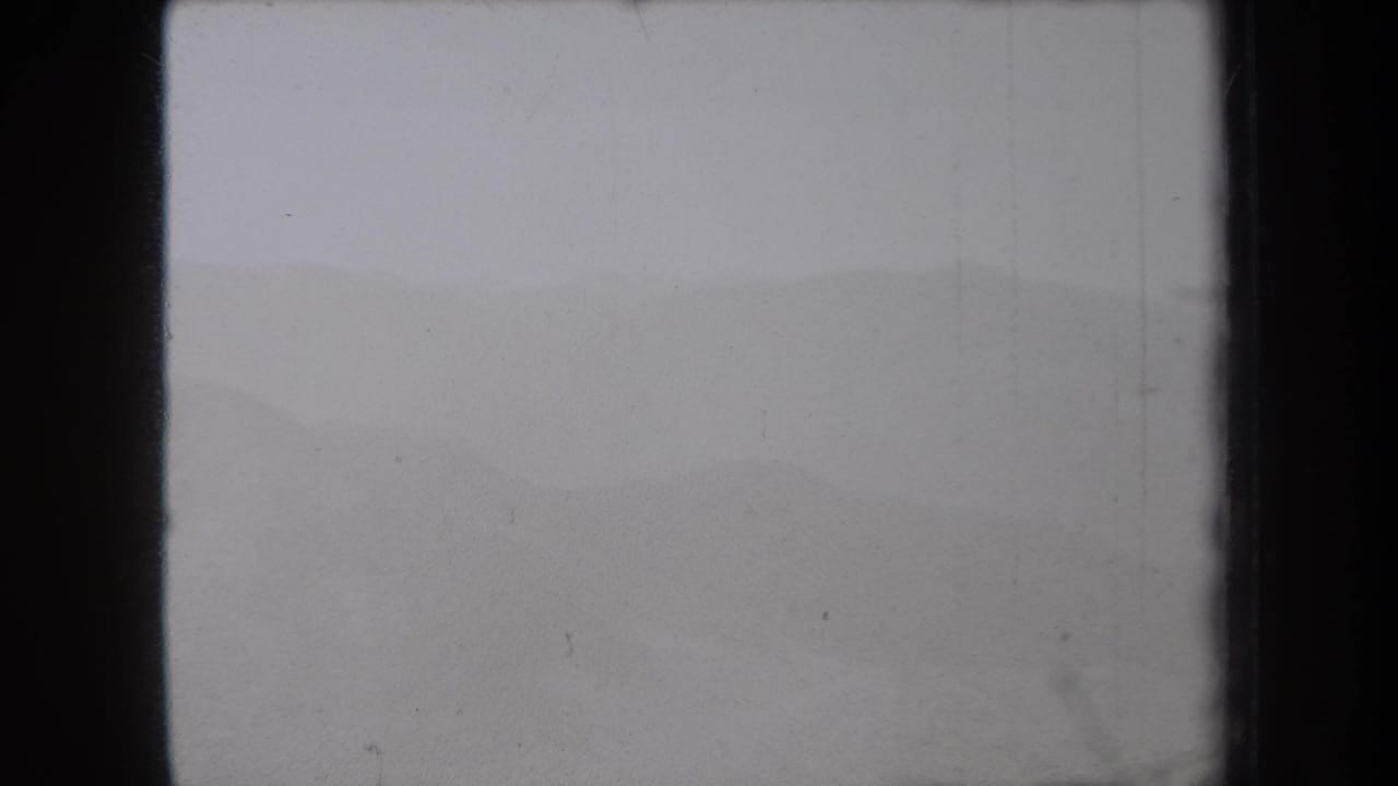 Fog-softened mountain slope under a pale gray sky with visible film borders.
