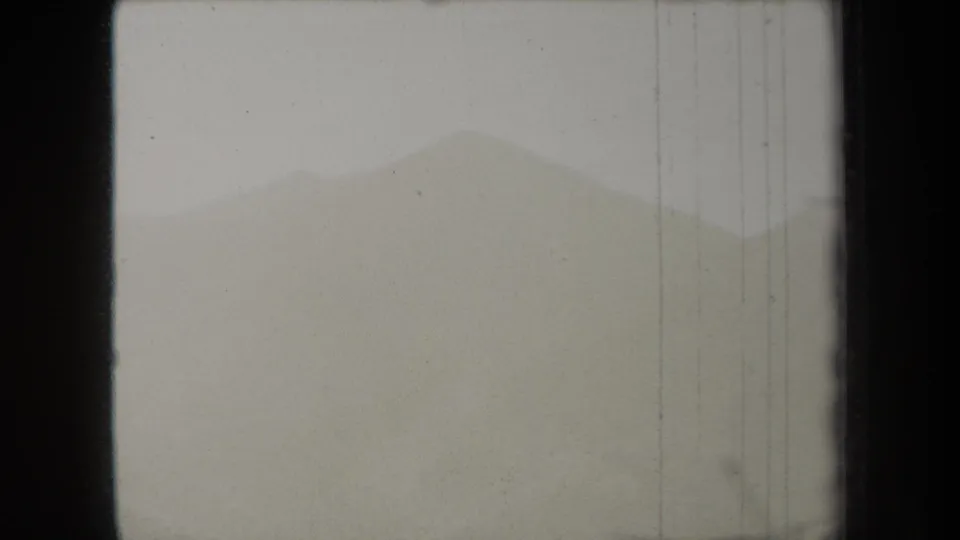 1938 8mm frame from New York metadata showing a hazy distant ridge with dark borders, scratches, and pale fog.