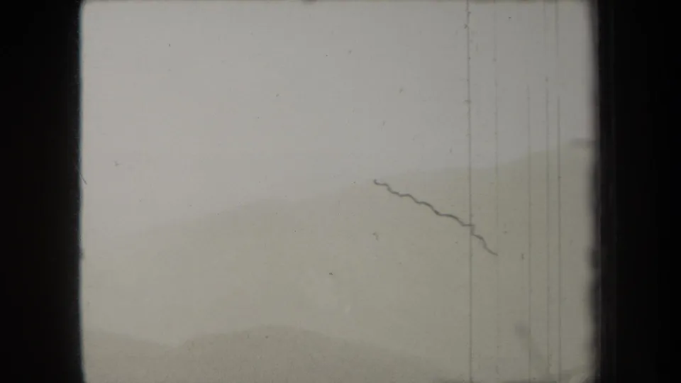 Monochrome 8mm frame from 1938 New York metadata showing washed-out fog, faint terrain, a dark scratch, and film-frame boundaries.