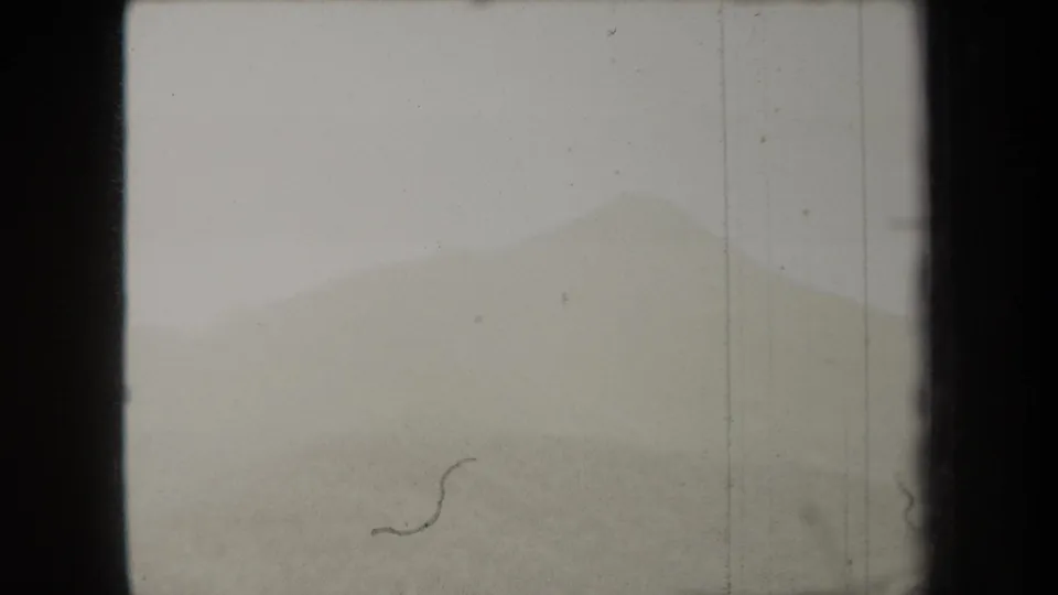 1938 New York 8mm frame showing a muted hillside silhouette, pale sky, dark edge framing, and visible dust on the film.