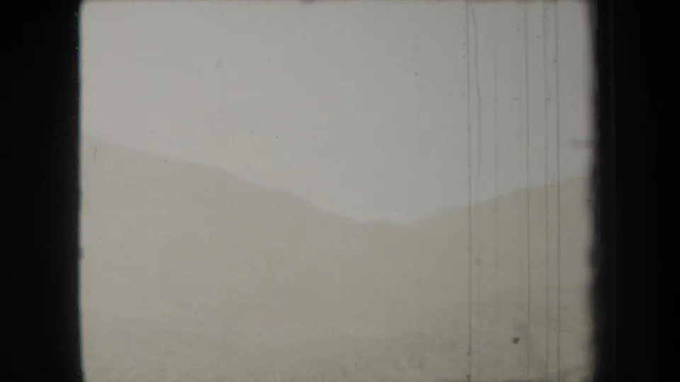 1938 New York 8mm frame with low hazy hills, a pale overexposed sky, dark film framing, and fine vertical scratches.