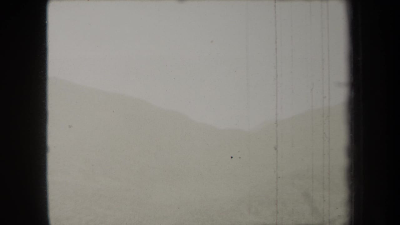 Pale hazy mountain ridges under an overexposed sky with dark film borders.