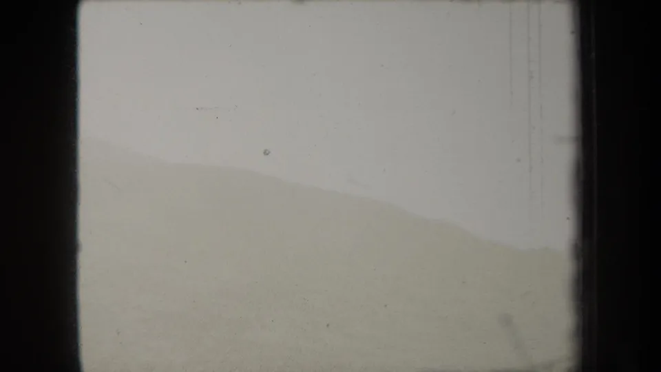 1938 New York home-movie frame with a muted mountain outline, bright sky, vertical scratches, and dark side borders.