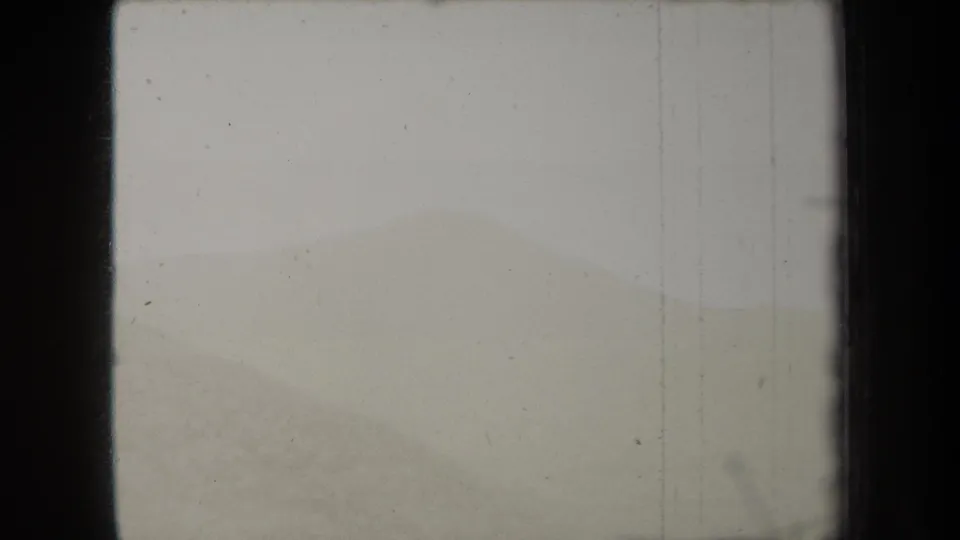 1938 New York home-movie frame with pale layered hills, an overexposed sky, vertical scratches, and edge shadowing.