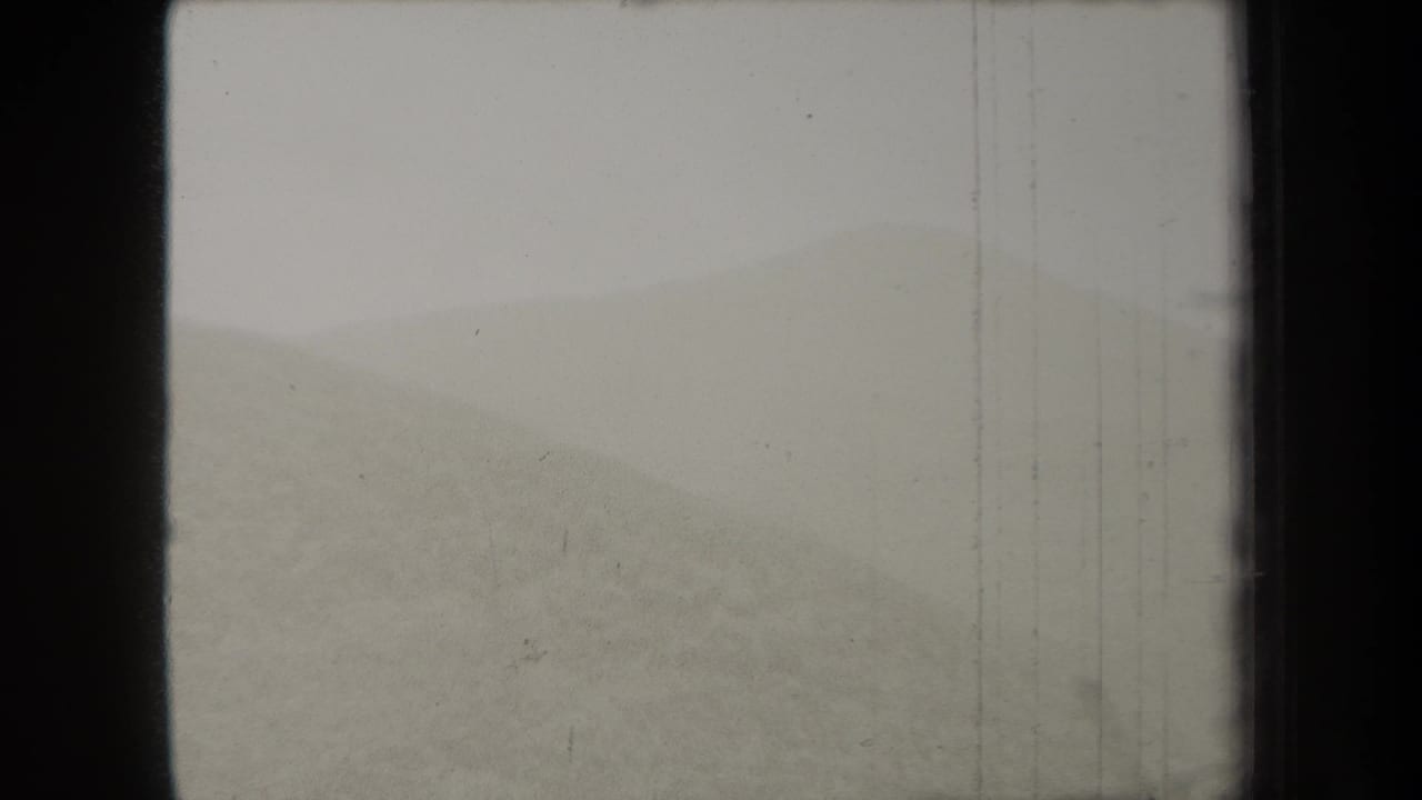 Hazy dune or low hill beneath a pale sky with dark film borders.