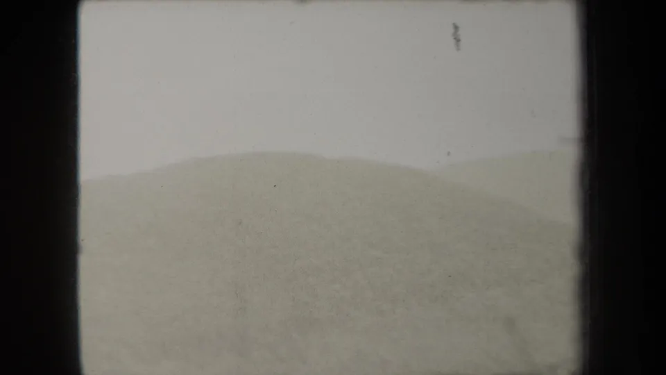 1938 New York home-movie frame with a rounded dune or low hill rising against a pale, featureless sky.