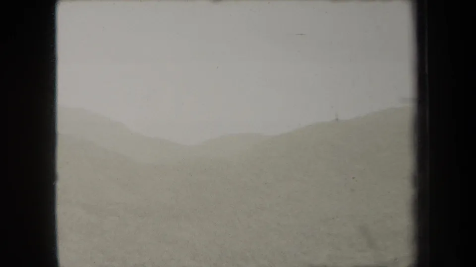 1938 New York home-movie frame showing open dunes or low hills, including a shallow dip between soft slopes under pale sky.