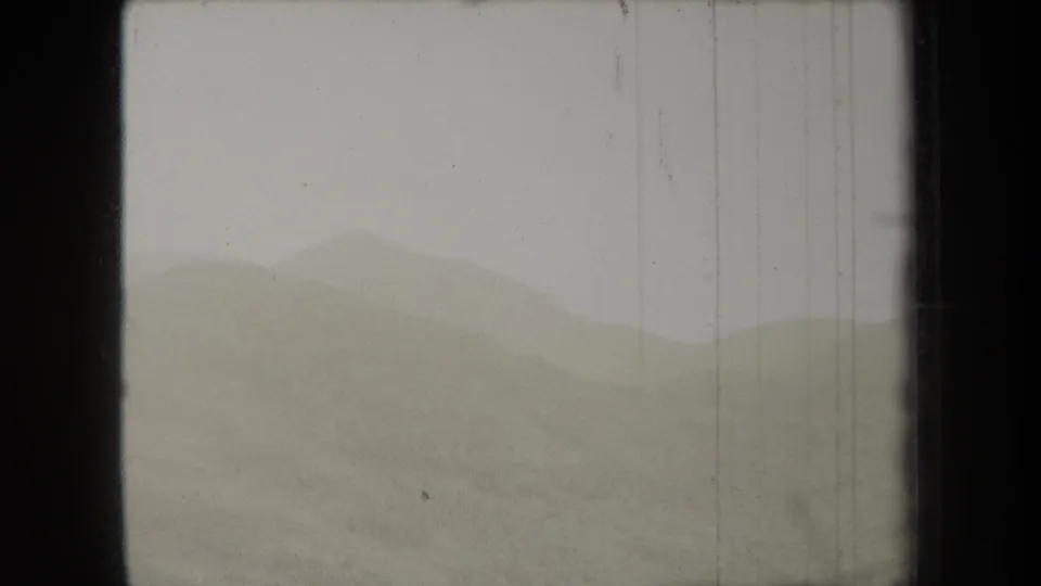 1938 New York 8mm frame showing distant hills or mountain forms partly obscured by haze beneath a flat gray sky.