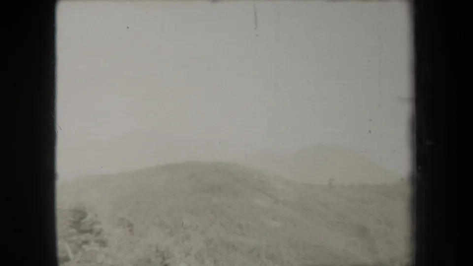 1938 New York home-movie frame with rounded tree-covered hills fading into fog beneath a pale sky.