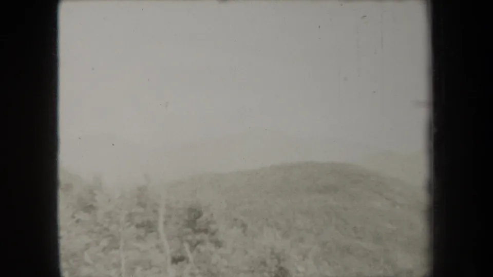 1938 New York 8mm still showing a misty wooded mountainside with pale sky and visible gate edges.