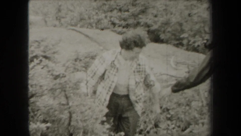 The 1938 New York footage shows a woman in a checkered shirt standing near brush in a wooded landscape.