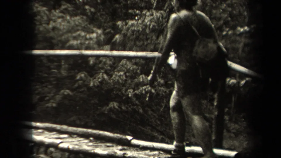 A woman walks across a simple wooden bridge in a wooded New York landscape, seen in 1938 home-movie footage.