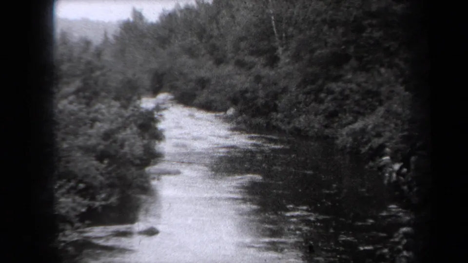 Black-and-white 8mm view of a river or stream running through wooded banks in New York, dated by metadata to 1938.