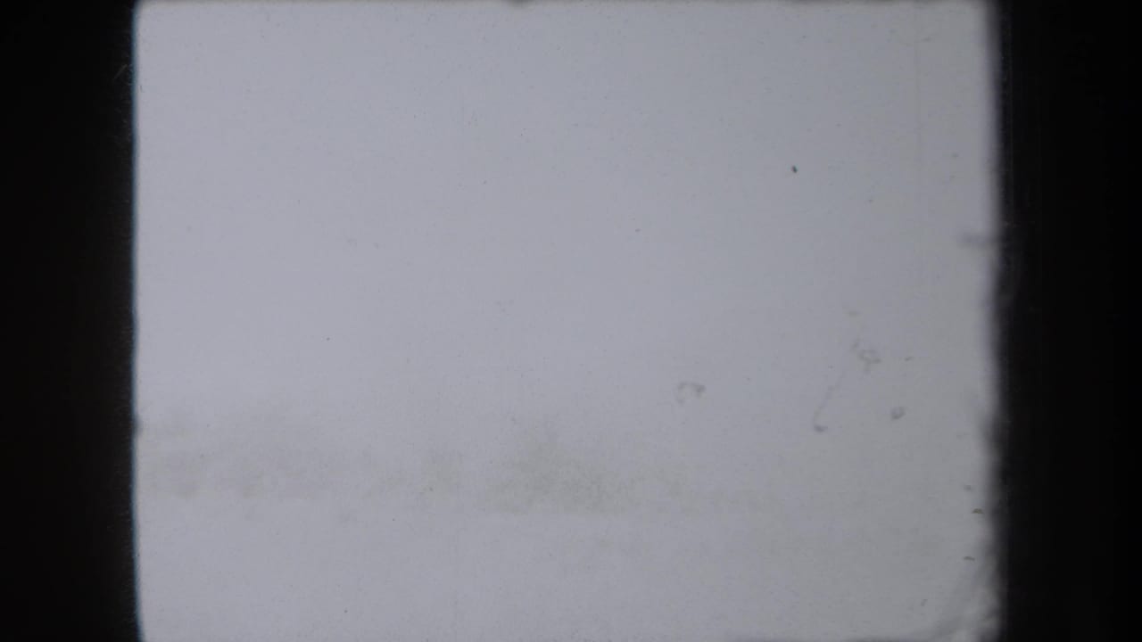 A mostly washed-out 8mm frame from the 1938 New York clip, showing dark frame edges and faint film specks before the stream view appears.