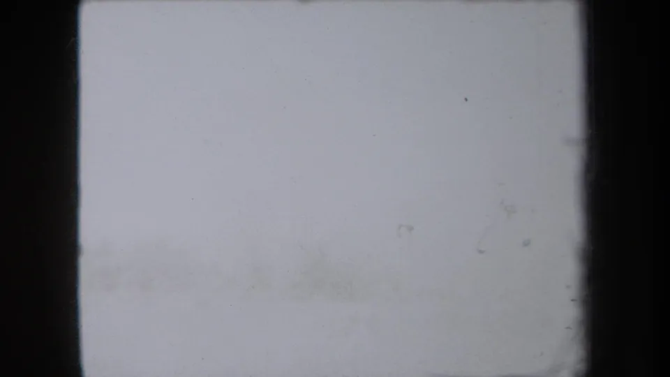 A mostly washed-out 8mm frame from the 1938 New York clip, showing dark frame edges and faint film specks before the stream view appears.