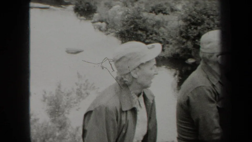 Black-and-white 1938 New York 8mm frame showing two adults near a creek, with the woman in profile and the second person partly visible.