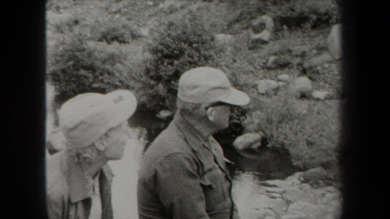 1938 New York 8mm frame of an older couple in hats standing outdoors near a small rocky creek.