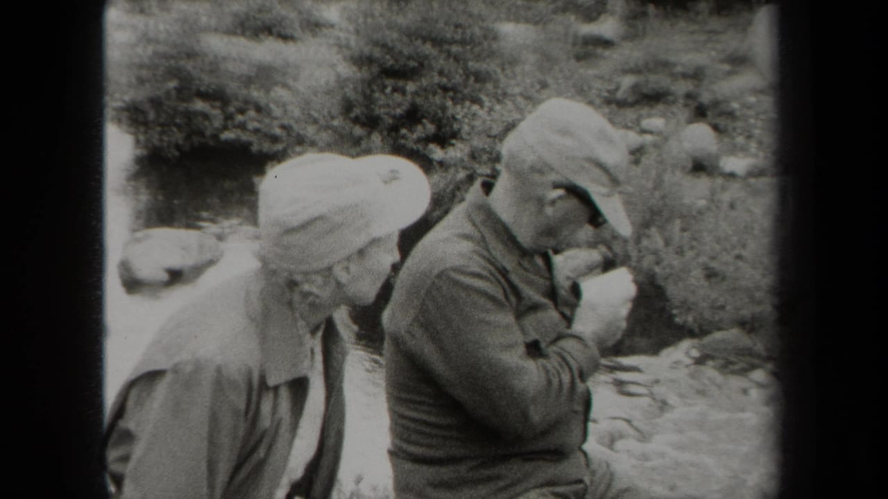 In metadata-supported 1938 New York, two uniformed men sit near a creek as one studies a folded paper or map.