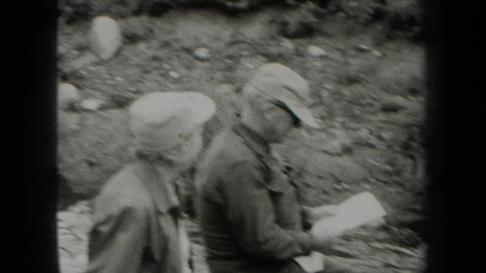 Two men sit near a rocky New York stream in 1938 home-movie footage, one turned away while holding a pale paper or object.