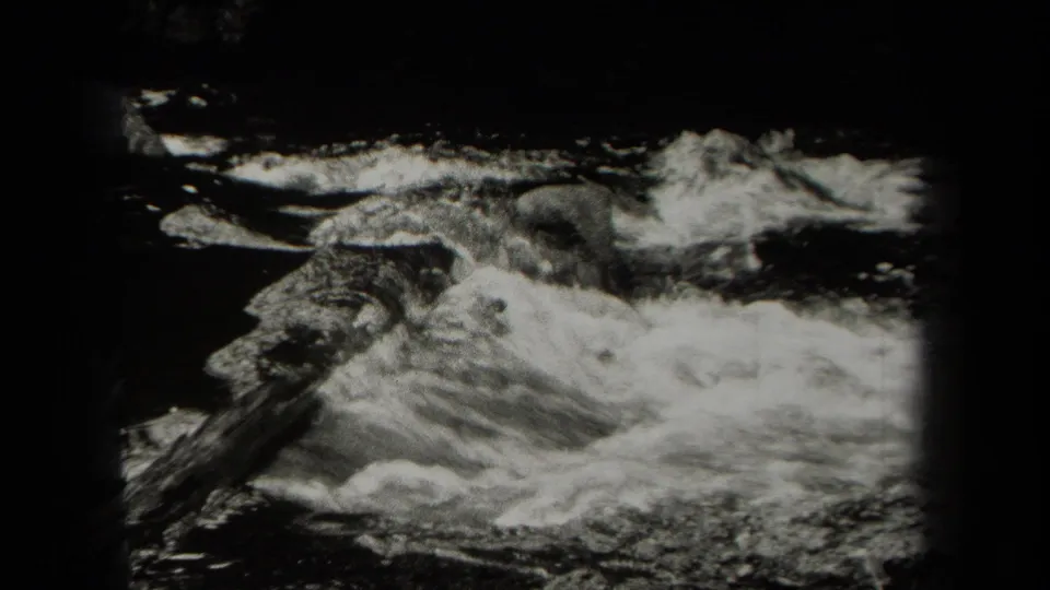 Foaming water rushes over rocks in a black-and-white 8mm frame, with dark gate edges and partial overlap from the contact sheet.