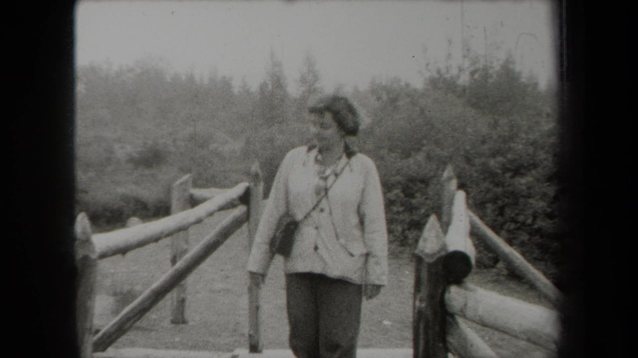 In metadata-supported 1938 New York footage, a woman stands near a rustic wooden fence in a wooded or landscaped area.