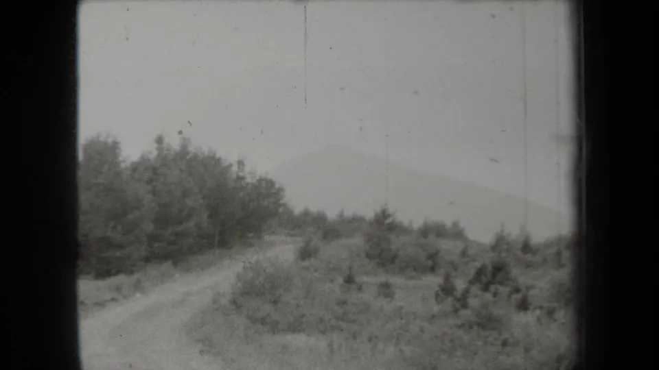 A rural New York dirt road winds through wooded brush toward a hazy distant mountain in 1938 8mm footage.