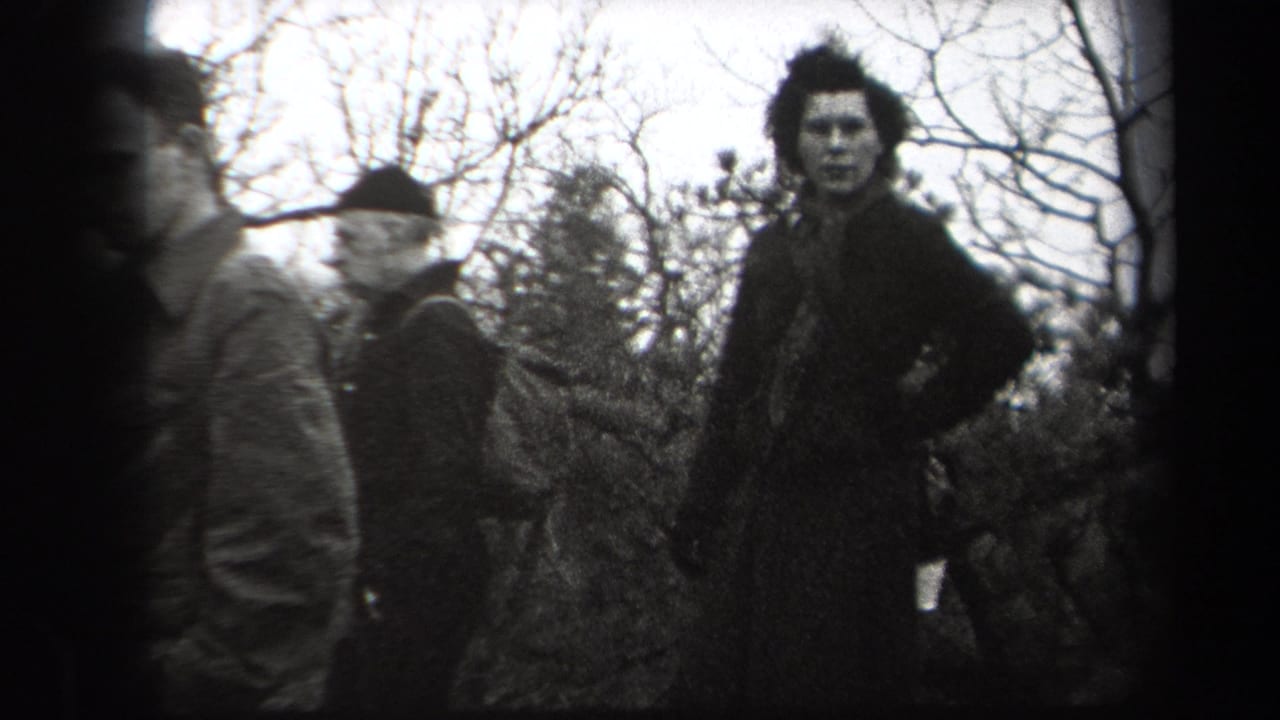 In 1938 New York home-movie footage, adult men in coats and hats gather in a wooded outdoor area while one man looks toward the camera.