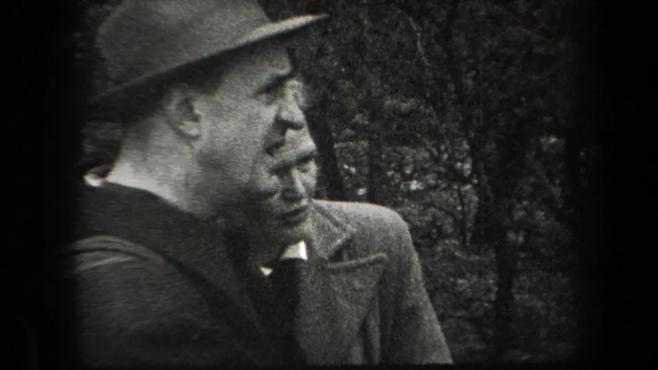 A man in a brimmed hat and heavy coat is seen in close profile outdoors, consistent with the 1938 New York home-movie setting.