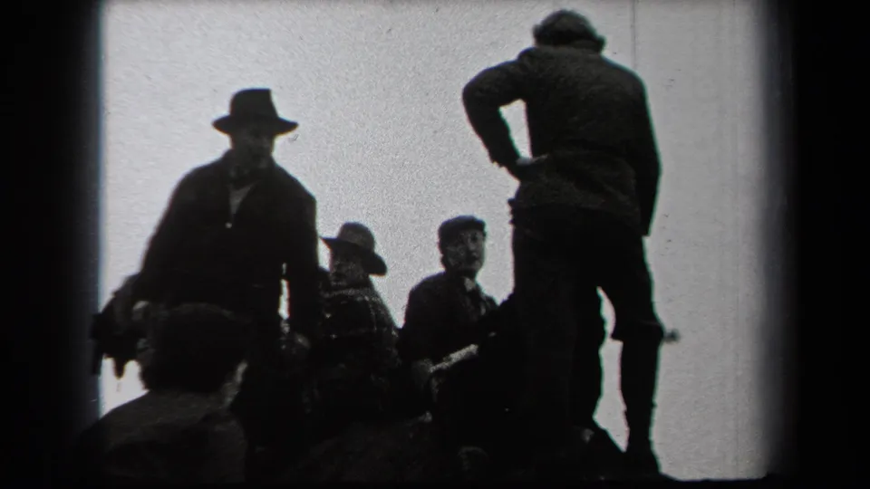 Backlit 1938 New York home-movie frame showing men in coats and hats gathered outdoors, with seated figures and one standing figure at right.