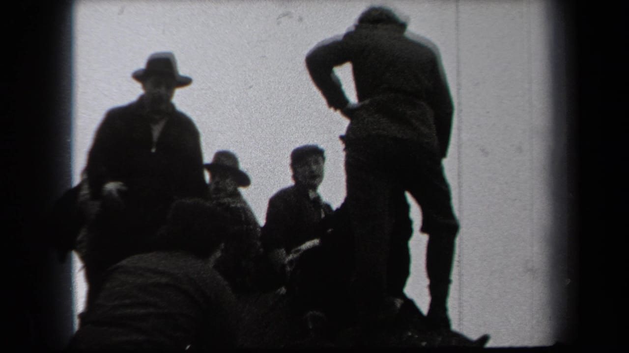Men in hats and overcoats stand and crouch against a bright sky at the edge of woods.